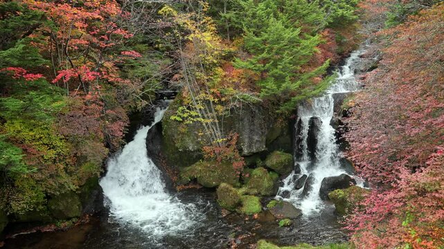 Beautiful waterfall flowing through rocks surrounded by vibrant autumn foliage in Nikko Japan scenic nature landscape