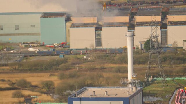 Biomass energy industrial facility. Waste wood slowly introduced to furnace with heat used to raise steam within the boiler then superheated and directed to steam turbine. Steam being released.