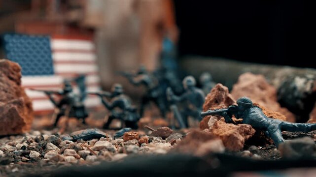 Miniature plastic soldiers representing an american army unit in a battle scene. The diorama features troops in combat with the us flag