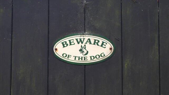 Oval beware of the dog warning sign on weathered wooden fence