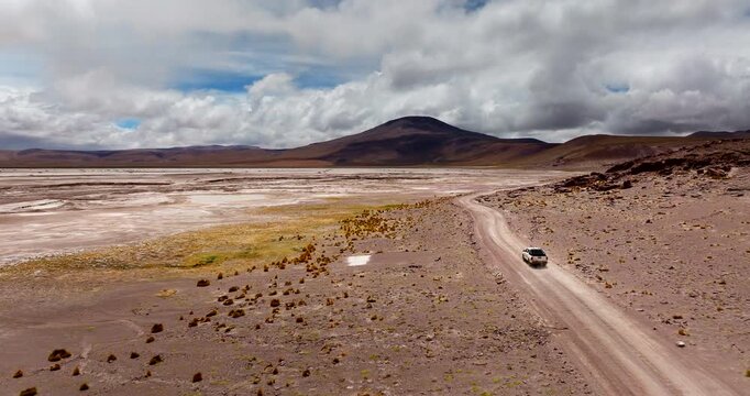 Aerial tracking follows vehicle driving on dirt road across Siloli Desert Bolivia, slow motion rearview