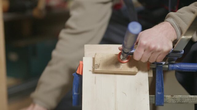 A woodworker's hands are shown tightening clamps on wooden pieces. The scene captures the careful process of securing wood with tools.