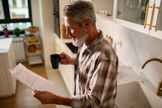 Senior man reading bills with coffee in home kitchen