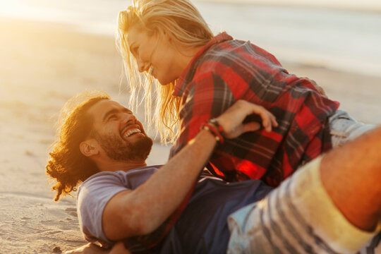 Happy couple laughing on sandy beach at sunset