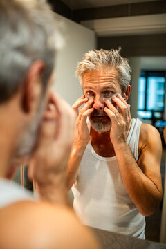 Mature man checking eye bags in bathroom mirror