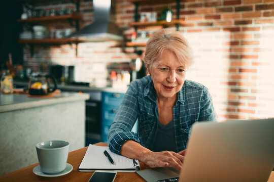 Smiling senior woman using laptop at home kitchen table