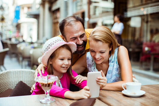 Happy family using smartphone at outdoor street cafe
