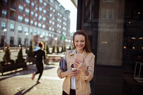 Smiling woman with coffee using smartphone on sunny city street