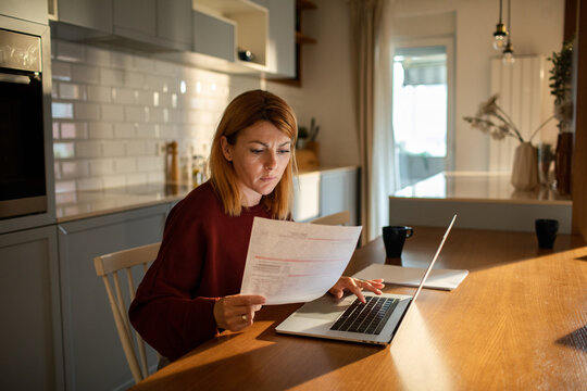 Woman reviewing bills on laptop at home kitchen table