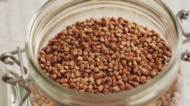 Close-up of buckwheat groats in a glass storage jar. Healthy food ingredient, kitchen storage and organic nutrition concept. High quality 4k footage