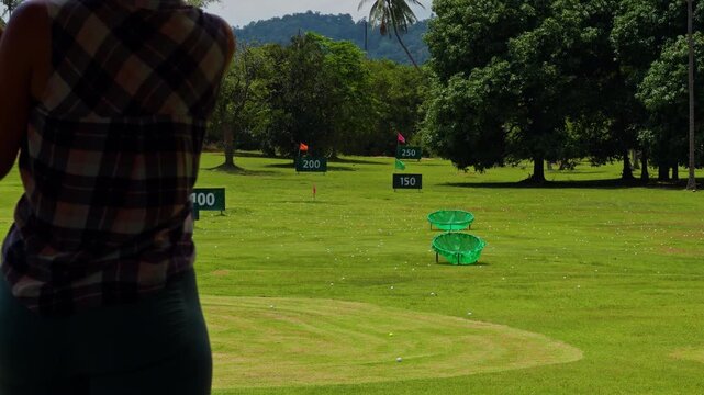 Woman hitting Golf ball on Driving range with distance marker and green basket in background, Dynamic Action and Precision