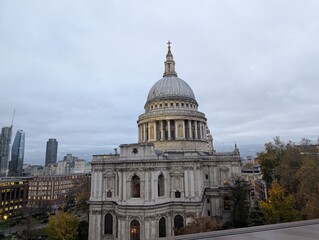 Obraz premium St. Paul's Cathedral in London overlooks a cityscape with autumn foliage and modern buildings under a cloudy sky.