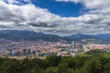 Fototapeta premium Espectacular vista aérea que revela el corazón de Bilbao, con la Ría del Nervión, el Museo Guggenheim y la Torre Iberdrola destacando bajo un cielo de nubes algodonosas y montañas imponentes