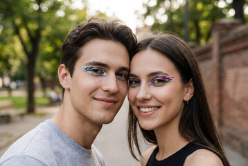 Naklejka premium Happy young couple with creative glitch eyeshadow and avant garde make-up editorial look posing together in sunny city park for modern lifestyle concept