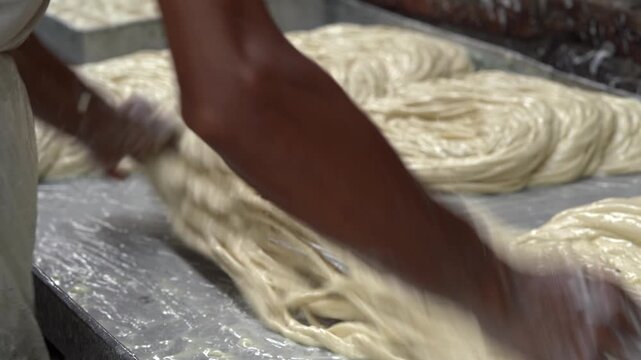 Street food cook hand kneading and stretching dough to make traditional feni, a vermicelli-like south asian sweet dessert made from flour, ghee, and sugar syrup