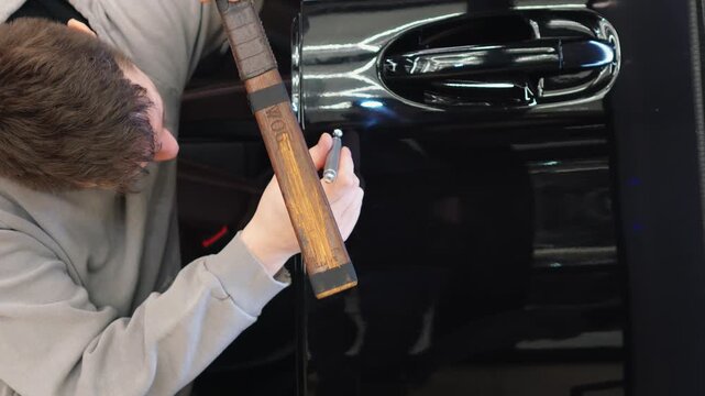 PDR. Process of paintless dent repair on car body. The mechanic at the auto shop with tools to repair dents in car body. Body repair. A specialist repairs a dent on the car body without painting. 