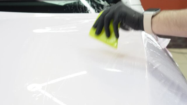 A specialist in wrapping a car with pink-chameleon vinyl film in the process of work. Car wrapping specialists cover the car with vinyl sheet or film. Car wrapping process. PPF protective film. 