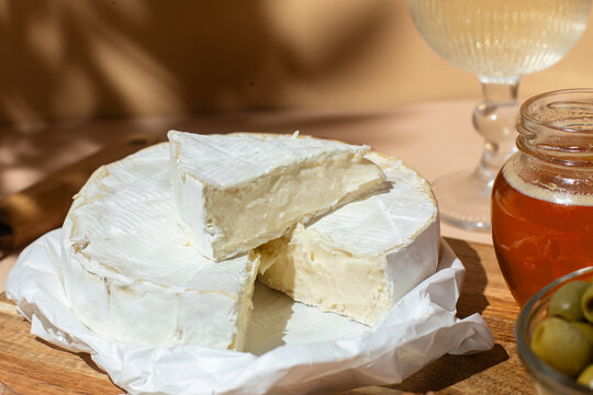 Gourmet Brie cheese platter with honey, green olives, and nuts on a wooden board. Sunny aesthetic with leaf shadows.