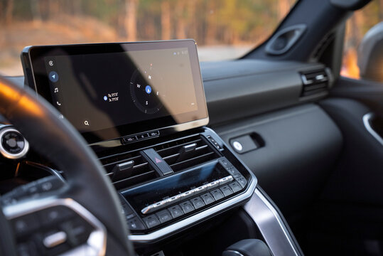 Modern car interior featuring a large floating touchscreen display with navigation, sleek air vents, and climate control buttons on a premium dashboard during sunset golden hour. High-tech cabin.