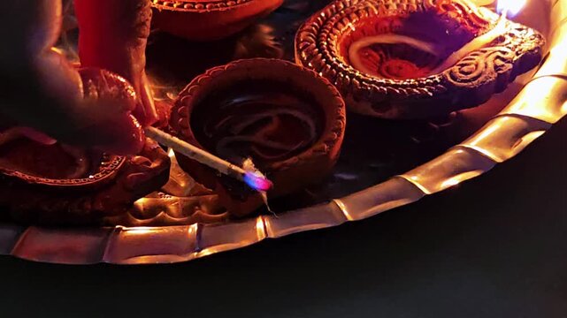A hand attempting to light traditional clay Diyas with a matchstick. Despite the effort, the match remains unlit, failing to ignite the oil lamps typically used to celebrate the festival of Diwali.