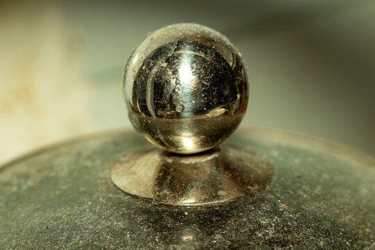 A shiny metal ball resting on a tarnished silver surface reflecting light detail