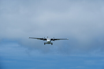 Fototapeta premium Twin-engine short-range transport aircraft on final approach to landing in blue sky with clouds. Regional twin-prop airplane landing in bright blue sky with fluffy clouds