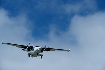 Fototapeta premium Twin-engine short-range transport aircraft on final approach to landing in blue sky with clouds. Regional twin-prop airplane landing in bright blue sky with fluffy clouds