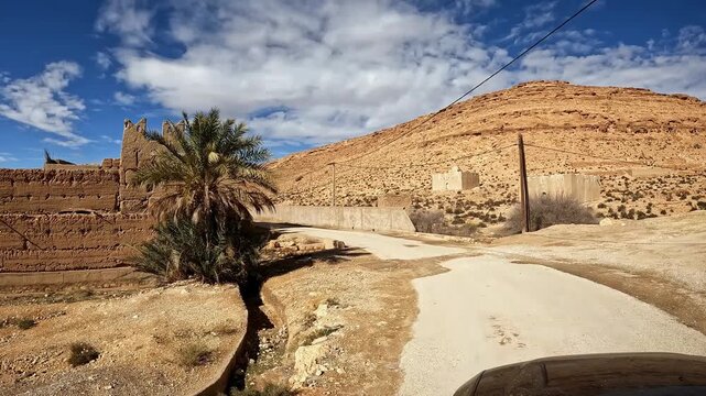 Car driving through an authentic moroccan kasbah village in the ziz valley oasis under a blue sky