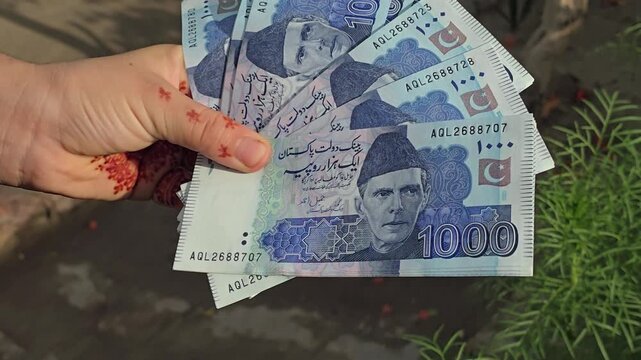 Pakistani one thousands  bank currency notes displayed in a hand featuring various denominations and designs of banknotes