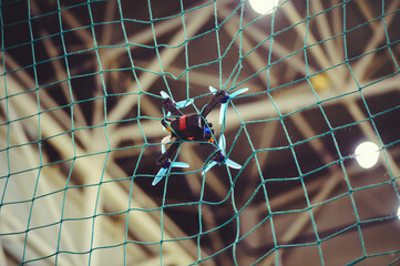 A horizontal shot of a small FPV racing drone with blue propellers stuck in a green safety net...
