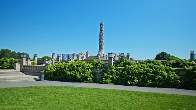 Scenic view across green lawns toward the Monolith sculpture in Frogner Park. Monolith tower and sculpture garden landscape during summer in Oslo, Norway.