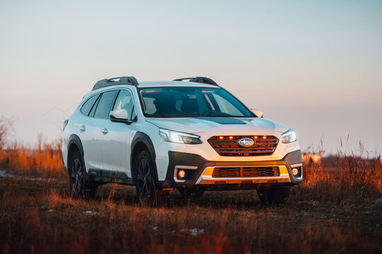 Brno, Czech Republic - February 10, 2026: White Subaru Outback SUV at sunset in winter on a field. Evening sky illuminated by orange light with a family Japanese SUV.