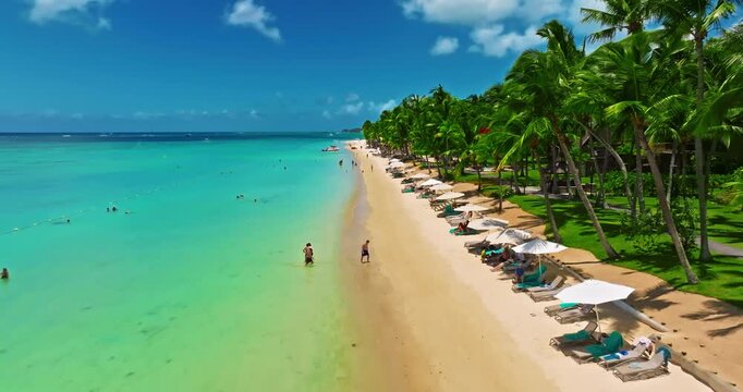Aerial view of beach with palm trees and perfect turquoise sea water. Relaxing and exotic drone view of a tropical coastline. Luxury summer vacation and holiday concept