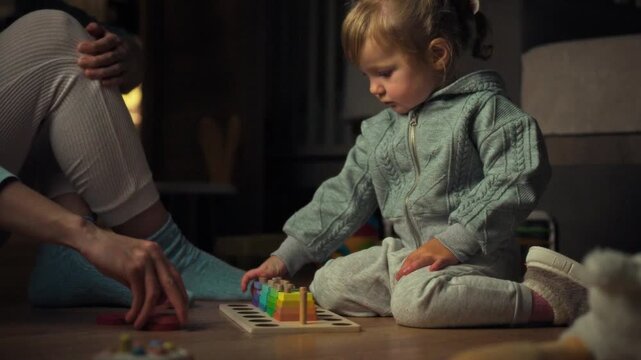 A young mother engages her little girl in assembling a colourful toy on the living room floor, showcasing a parents involvement in their childs early development and learning experience within a warm