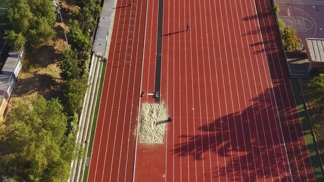 Person jumping hurdles on red running track and a long jump sandpit. Chile, 4K