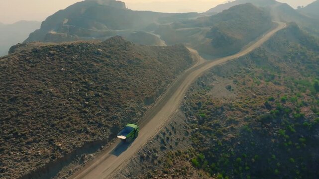 An aerial shot of a green-coloured EV mining dump truck climbing a mountain in Pakistan.