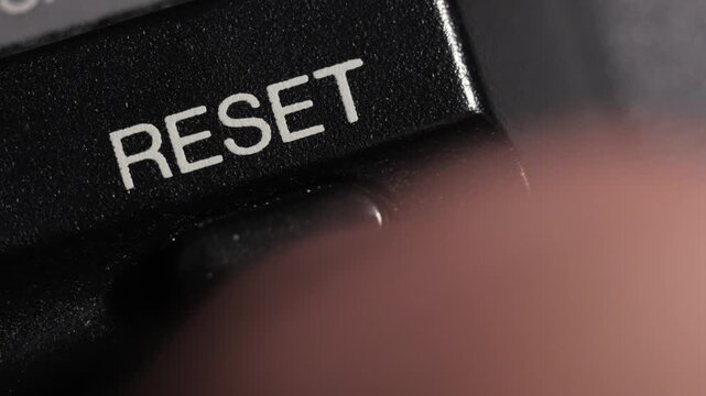 Diagonal macro close up of finger pressing black reset button symbolizing restart and renewal