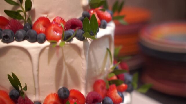 A delightful, lush two-tiered white cake, generously topped and layered with a colorful mix of fresh berries, cherries, and orange physalis