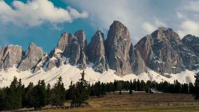 Steep limestone Dolomite pinnacles with forest below under blue sky, Zanser Alm region, Italy, panning