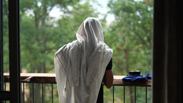 Man praying with tallit facing nature, gently swaying during prayer.