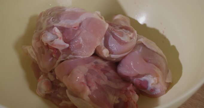 Female chef's hands seasoning raw chicken thighs with a mix of spices and herbs in a bowl, preparing the meat for cooking a delicious and healthy homemade meal for lunch or dinner.