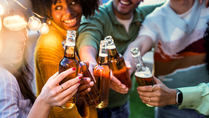 Obraz premium Happy friends enjoying night party on rooftop terrace - Group of multiracial young people drinking beer bottle at brewery pub garden - Life style concept with guys and girls hanging outdoors