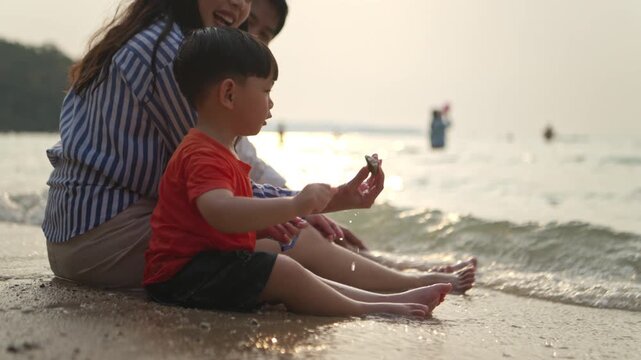 The little child sits on the beach at sunset, throwing stones while their mother and father sit beside them