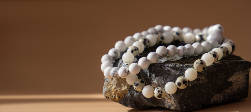 Men's beaded bracelets made of natural Dalmatian jasper and white howlite on a dark stone podium. Banner, copy space beige background