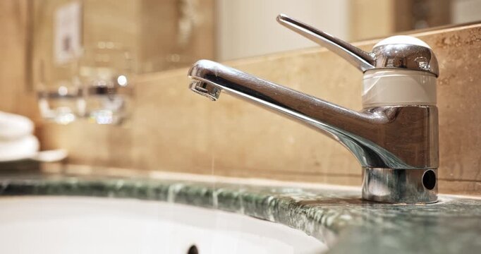 Modern chrome lever tap dripping water into a green marble vanity sink in a bathroom. Close up shot, shallow depth of field, real time video