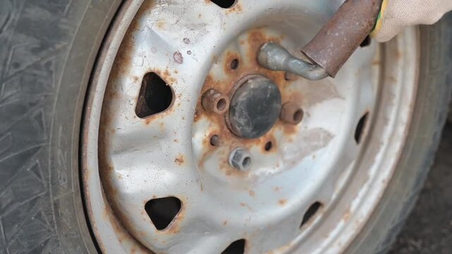 Close-up view of a rusty wheel rim with a tool engaged in removing a lug nut. The rusty bolt and nut won't unscrew.