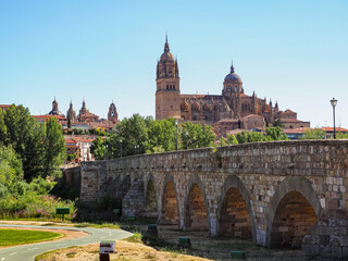 Obraz premium Panoramic view of Salamanca. Roman pedestrian bridge Puente Romano and famous old town with ancient buildings. Impressing old and grand new Cathedral of Salamanca, baroque cupola and tall bell tower.