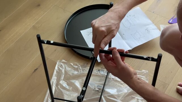 Hands continue assembling coffee table and tighten bolt with hex tool. Fingers fix frame parts using metal key during furniture setup. Concept diy, home, assembly, interior..