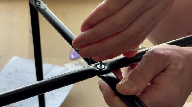 Hands tighten bolt in metal frame using hex key during table assembly. Fingers secure connection of parts while building furniture at home. Concept diy, interior, setup..