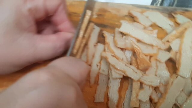close up of a hand holding a wooden board. Slicing Fish Balls for Cooking Ingredients